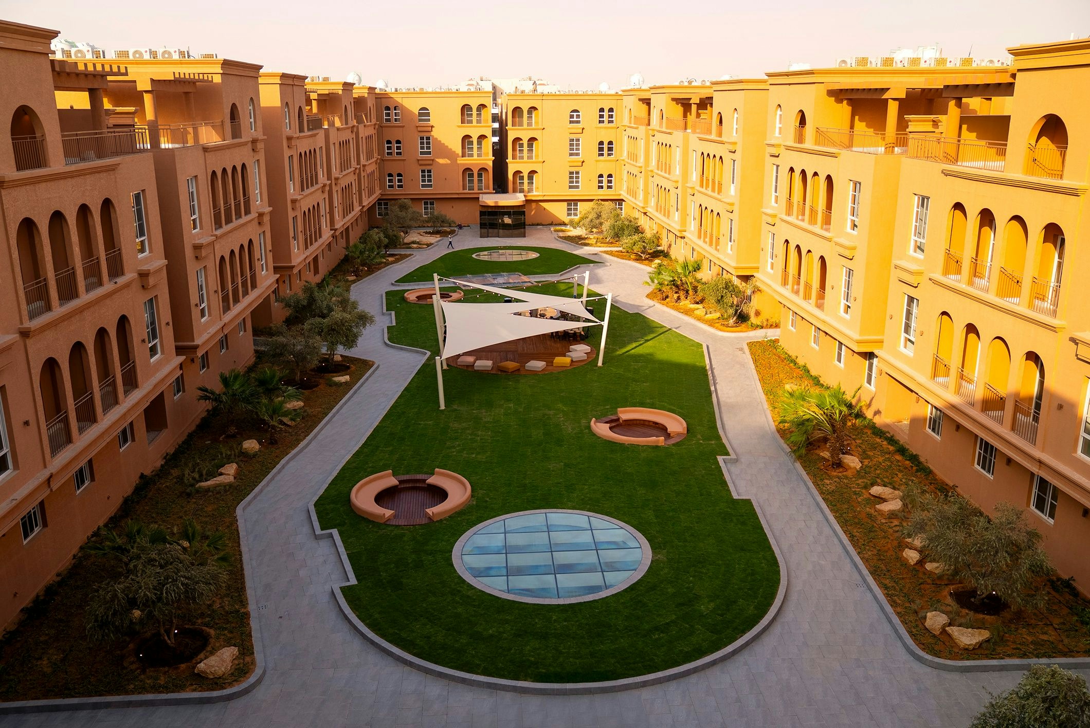 Sun rises on a courtyard at Flow Granada filled with plants, indented seating areas, turf, and walkways