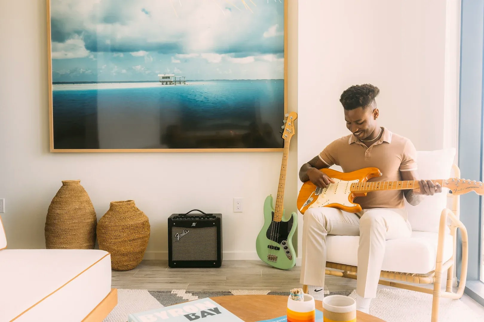 A man strums a guitar in an apartment living room next to wall art of an ocean